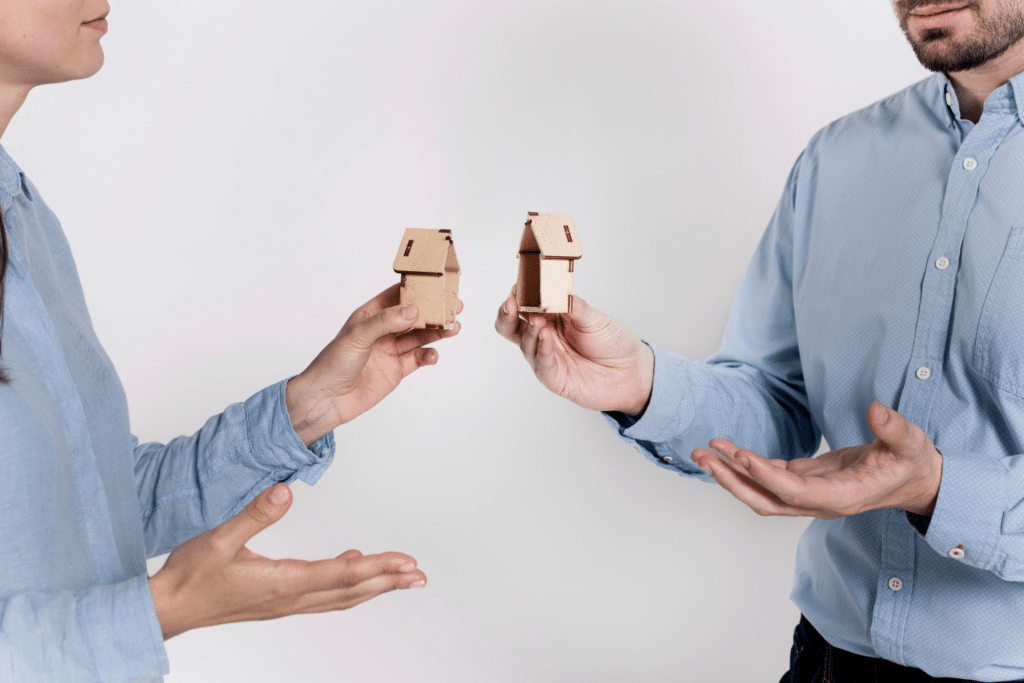 Two individuals holding divided wooden house models, symbolizing estate division between siblings.